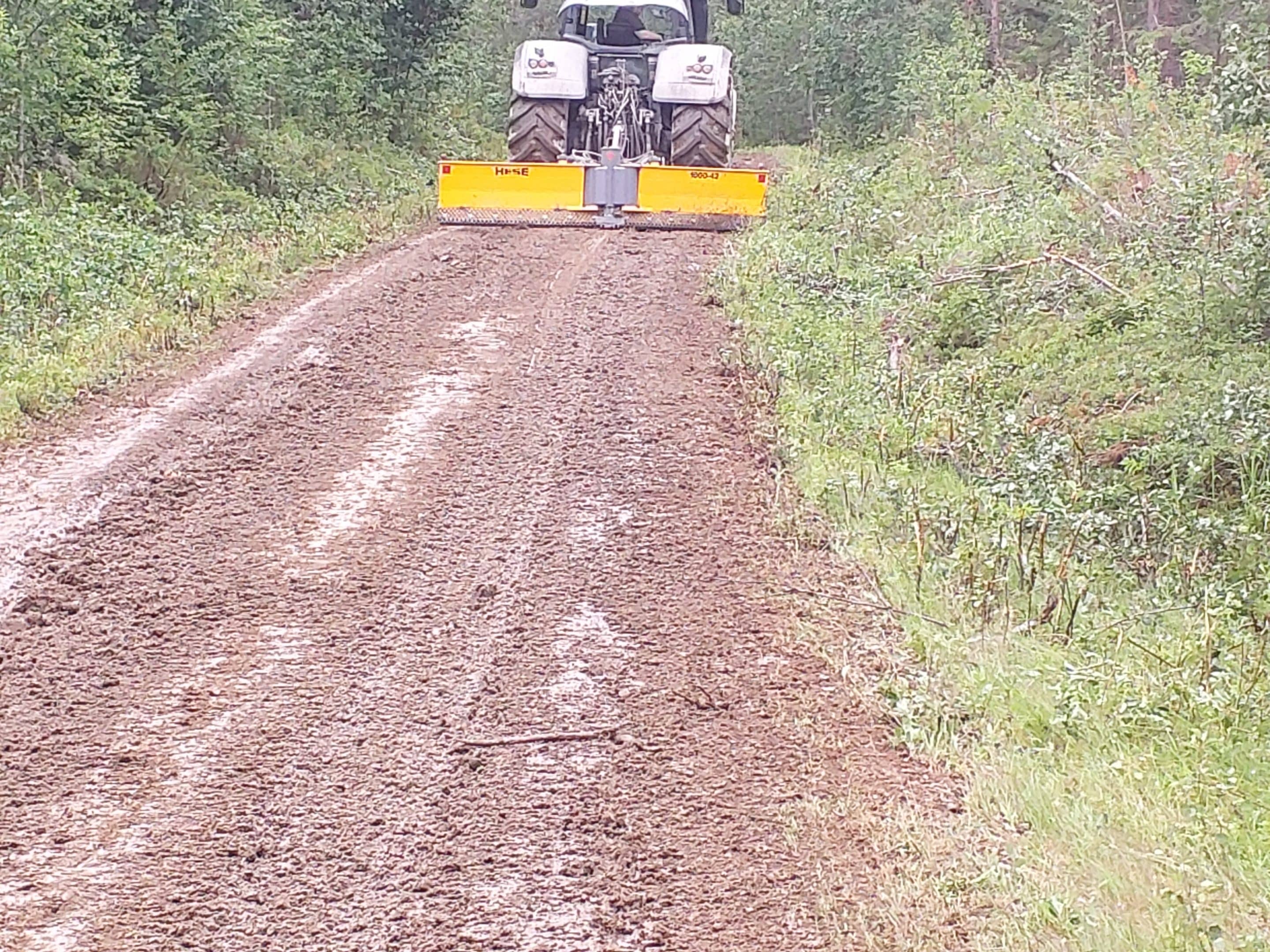 Traktori vetaa lanaajaa perassa hiekkatiella.